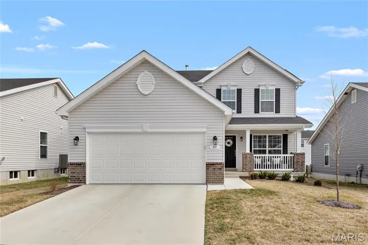 Traditional-style home featuring covered porch, brick siding, a front lawn, concrete driveway, and an attached garage