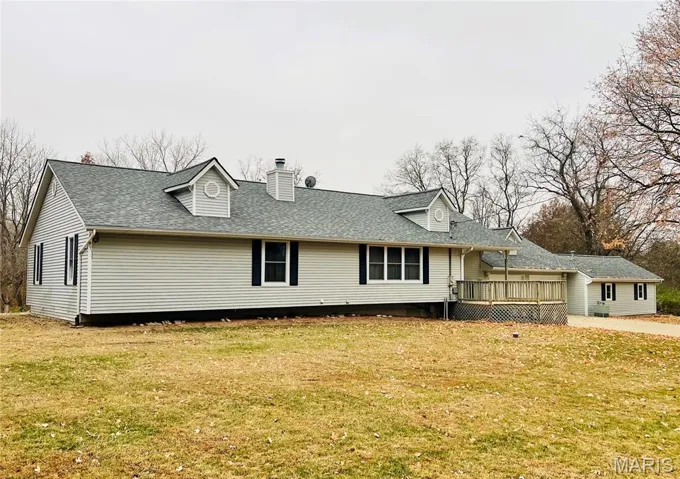 View of front facade with a chimney, a deck, a front yard, and roof with shingles