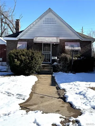View of front of house featuring brick siding and a chimney