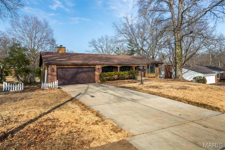 Single story home with concrete driveway, brick siding, an attached garage, and a chimney