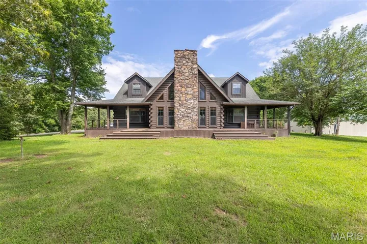 Back of property with log siding, a chimney, a lawn, and a porch
