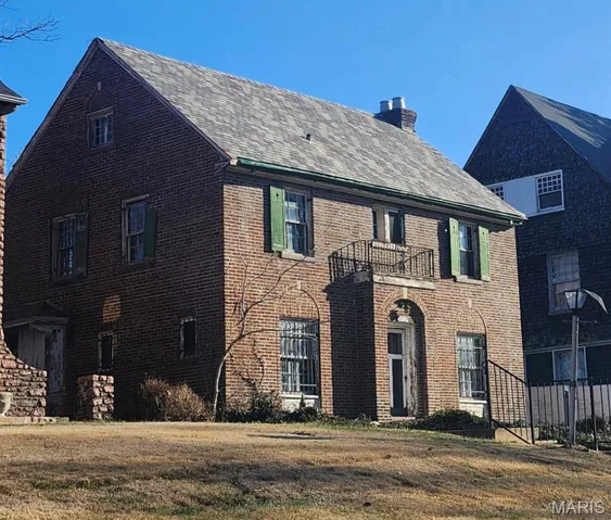 View of front of house featuring a balcony, a chimney, brick siding, and a front lawn