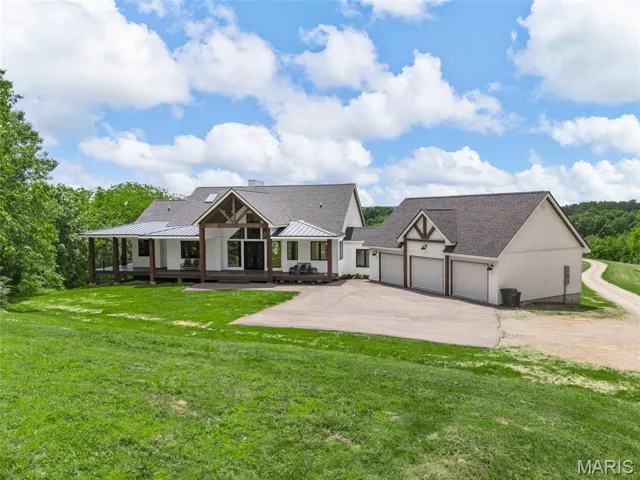 Back of property featuring asphalt driveway, an attached garage, a lawn, a shingled roof, and a standing seam roof