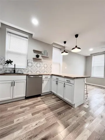 Kitchen with decorative light fixtures, a peninsula, white cabinetry, and light wood-type flooring