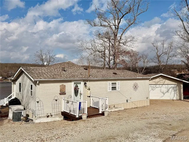 Front of property featuring a wooden deck, roof with shingles, a garage.