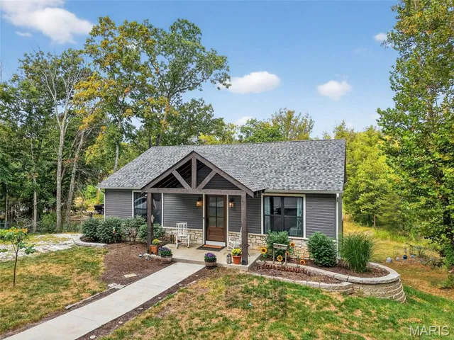 Bungalow with a porch, stone siding, a shingled roof, a front yard, and view of scattered trees