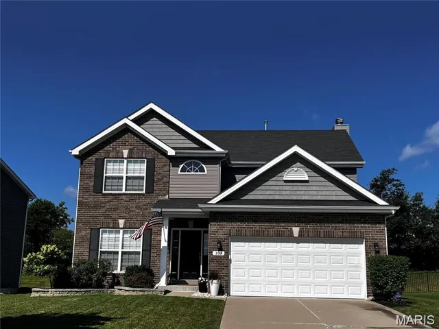 Traditional-style house featuring driveway, a front lawn, brick siding, and a garage