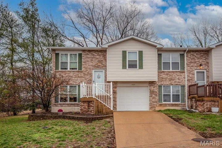 Raised ranch featuring concrete driveway, brick siding, a garage, and a front yard