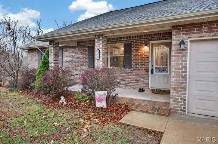 Property entrance featuring a porch, brick siding, a shingled roof, and an attached garage