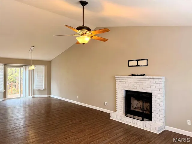Unfurnished living room featuring dark wood finished floors, vaulted ceiling, a brick fireplace, and a ceiling fan