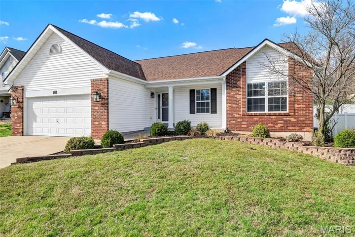 Ranch-style home featuring a front yard, an attached garage, driveway, brick siding, and roof with shingles