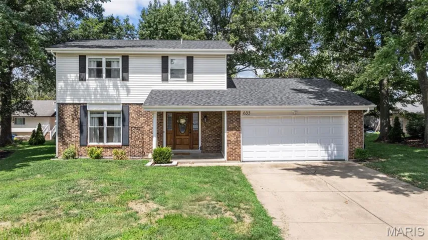 Traditional-style home featuring brick siding, concrete driveway, a front lawn, a garage, and roof with shingles