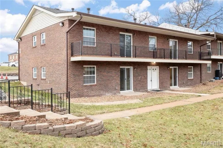 Back of house featuring a balcony, brick siding, and a yard