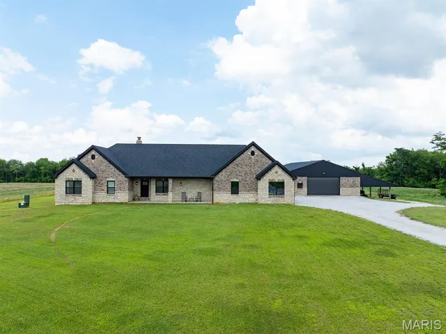 French country style house featuring a front lawn, stone siding, gravel driveway, and a chimney