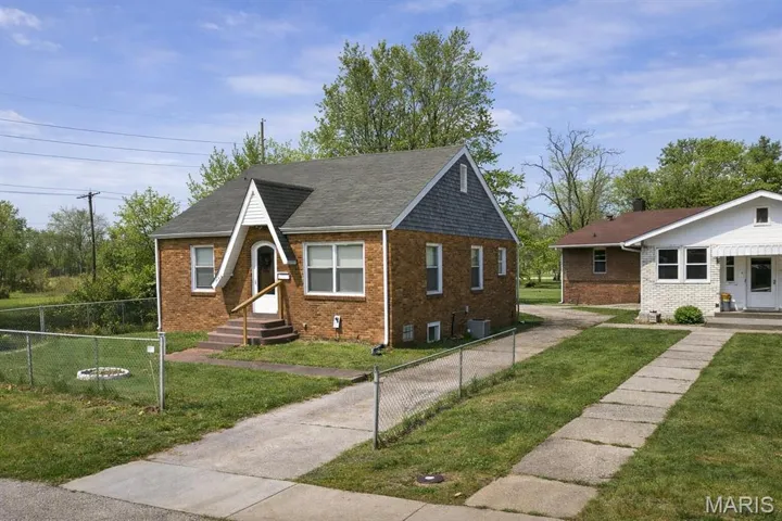 Bungalow-style home featuring brick siding, a fenced front yard, and a shingled roof