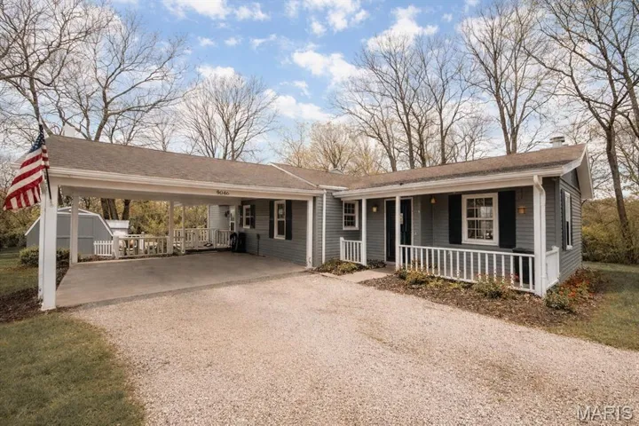 Ranch-style home with gravel driveway, an attached carport, a chimney, and a porch