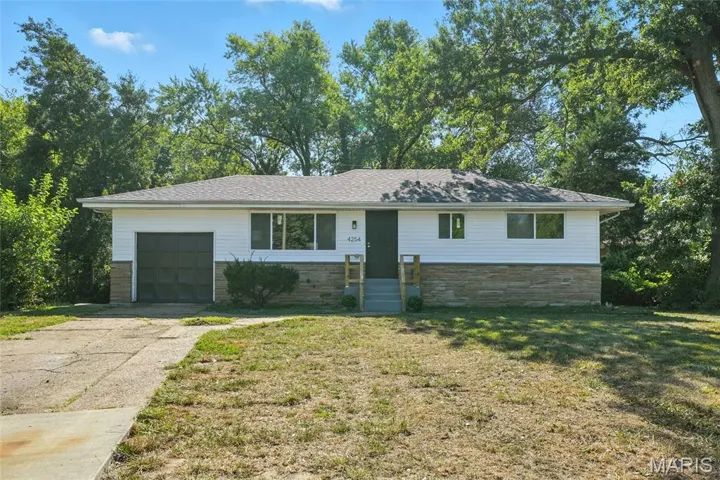 Ranch-style home with stone siding, a front yard, concrete driveway, and a garage