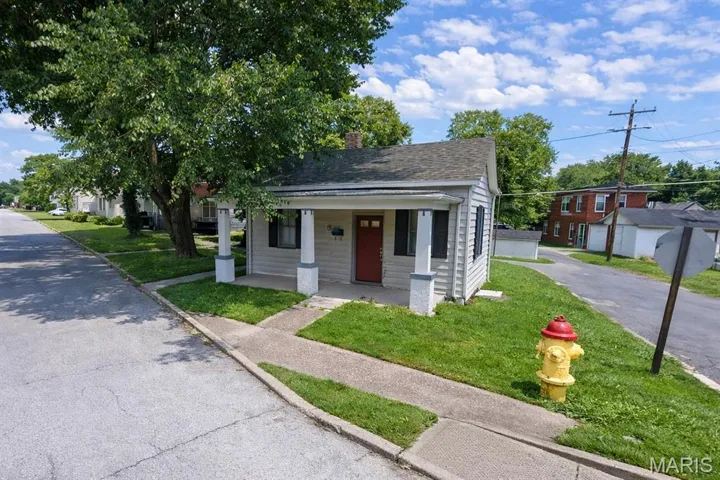 Bungalow-style home with covered porch, a front lawn, a chimney, and a shingled roof