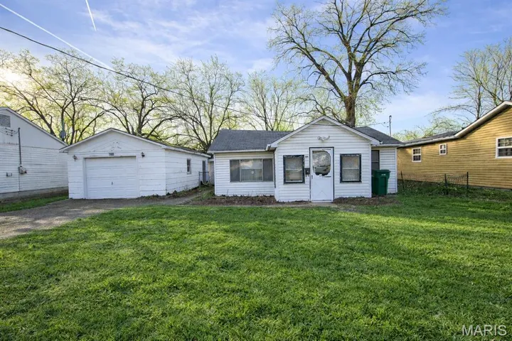 View of front of house with a detached garage, driveway, an outdoor structure, and a front yard