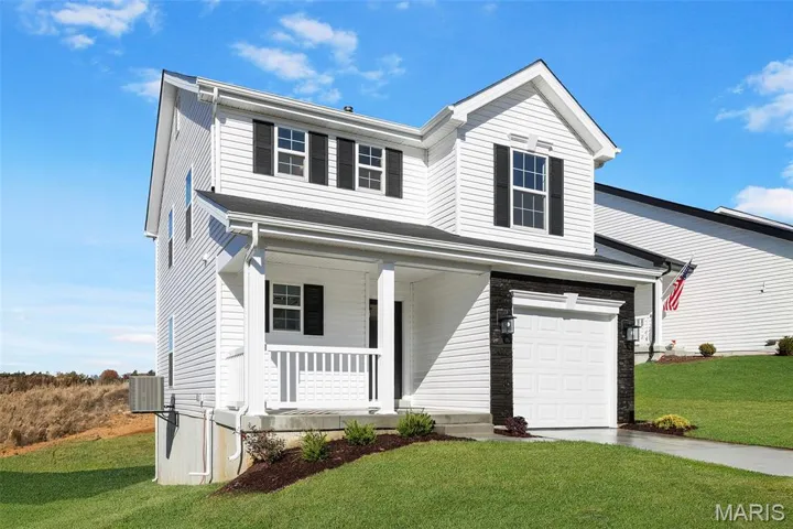 Traditional-style home featuring a front lawn, a porch, concrete driveway, and a garage