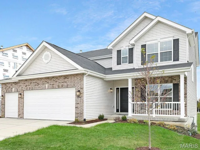 Traditional-style house with a porch, a front yard, driveway, an attached garage, and brick siding