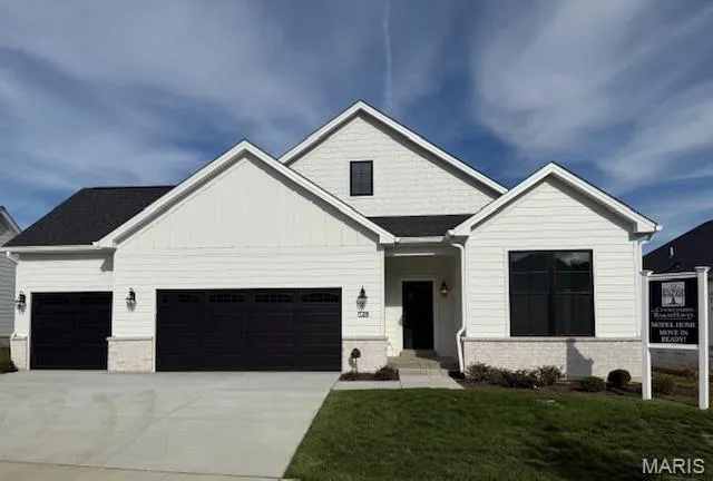 View of front of house featuring board and batten siding, concrete driveway, a front lawn, a garage, and brick siding