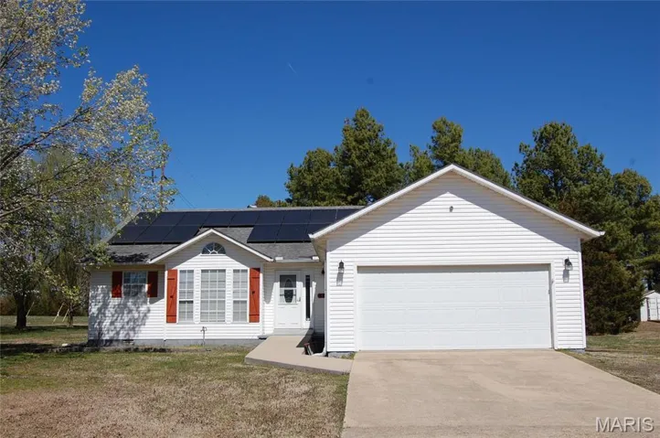 Single story home featuring a front yard, roof with shingles, concrete driveway, an attached garage, and solar panels