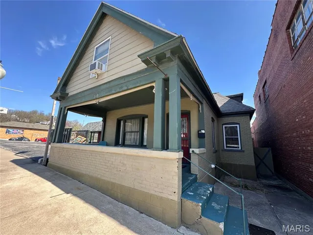 View of front of house featuring cooling unit, brick siding, and a porch