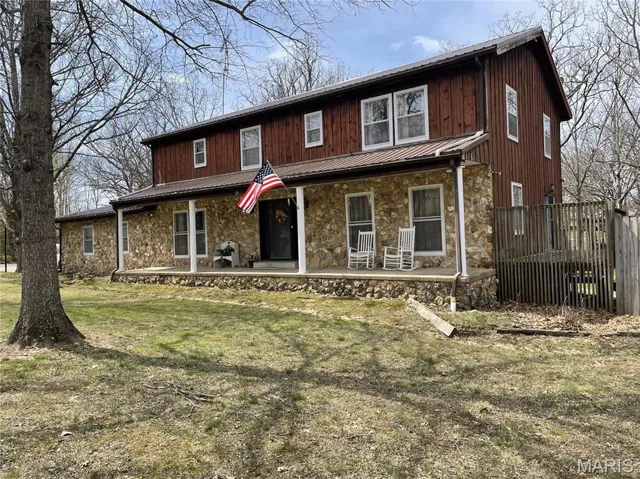 View of front of home with a front yard, a standing seam roof, stone siding, board and batten siding, and metal roof