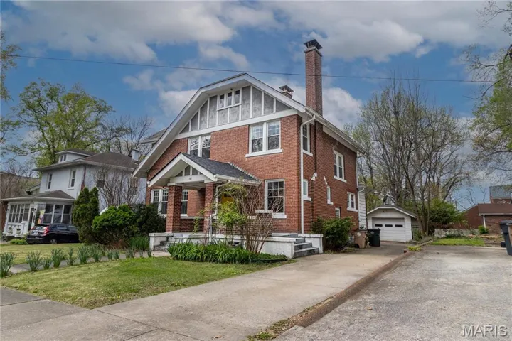View of front facade featuring an outbuilding, brick siding, a chimney, a garage, and driveway