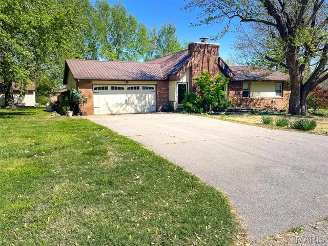 Ranch-style home with a front yard, an attached garage, a chimney, brick siding, and driveway