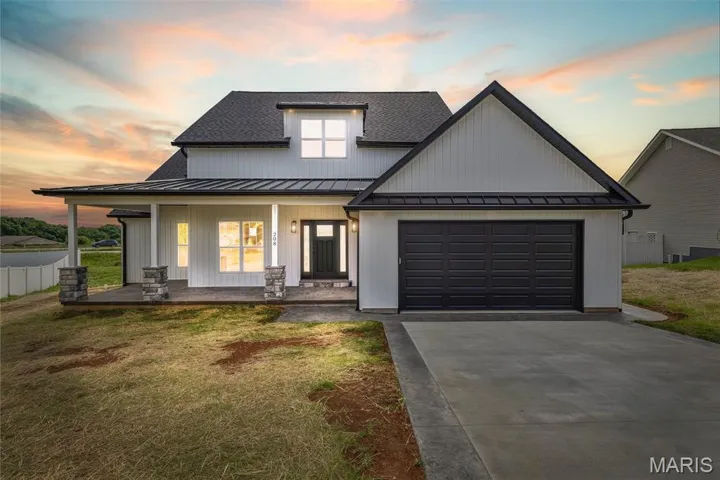 Modern inspired farmhouse with a standing seam roof, a porch, concrete driveway, an attached garage, and a front yard
