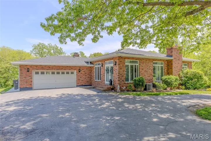 View of front of home featuring a chimney, driveway, brick siding, an attached garage, and a shingled roof