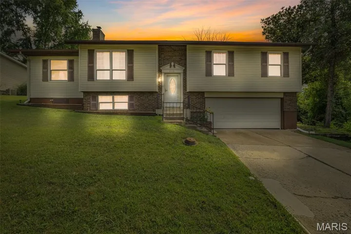 Raised ranch featuring driveway, a front yard, a garage, brick siding, and a chimney