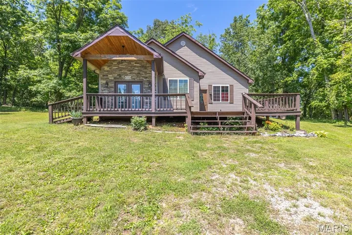 Back of house with stone siding, a wooden deck, and a yard