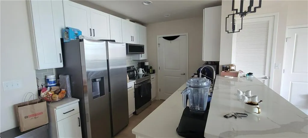 Kitchen featuring white cabinetry, backsplash, light stone counters, and appliances with stainless steel finishes