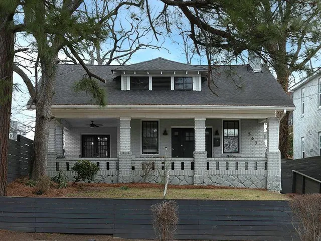 Gray brick facade with stone foundation accents, featuring a deep covered porch with square columns