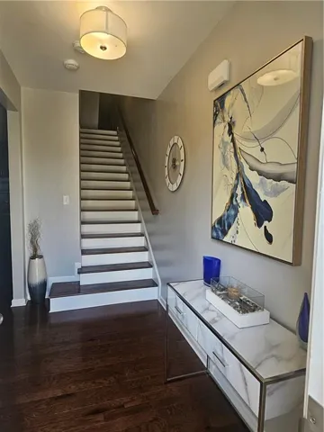 Wood-finish flooring, staircase with wood risers, modern drum pendant light fixture, and a console with a marble-look top