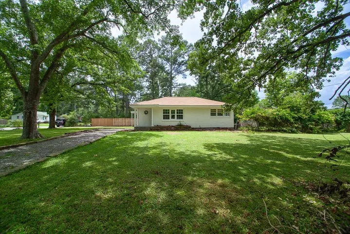 Expansive front lawn with mature trees, gravel driveway, and a white brick exterior