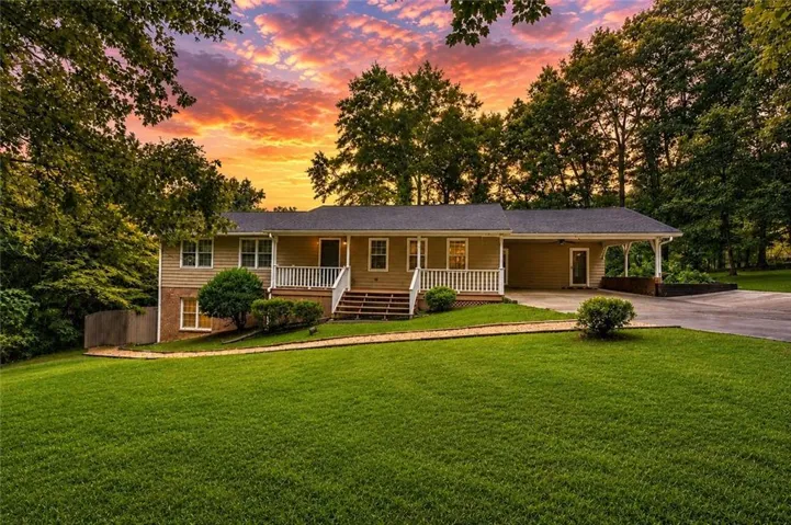 Split-level residence featuring a covered entry porch with white railings, a front-facing carport, and a sloped front yard with a paved driveway