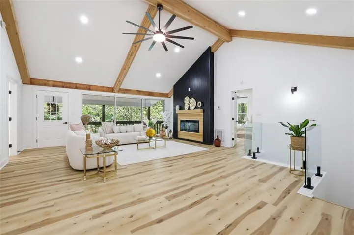 Vaulted ceiling with exposed wood beams, wood-finish flooring, built-in fireplace, recessed lighting, and a glass panel railing
