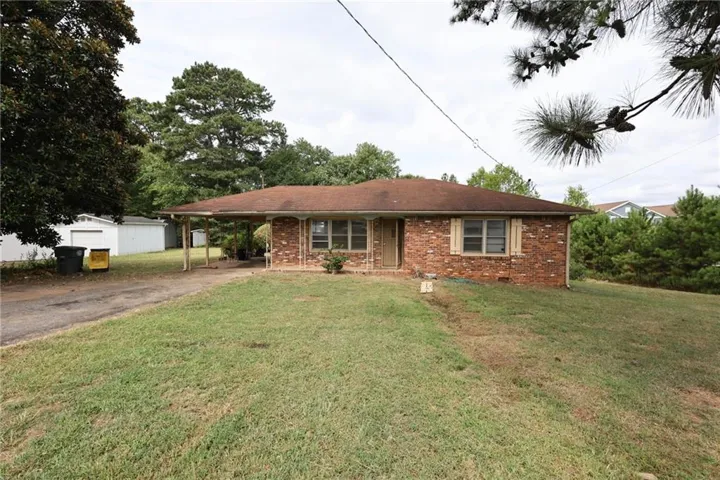 Brick exterior, covered carport, shingle roof, established landscaping, and detached outbuilding