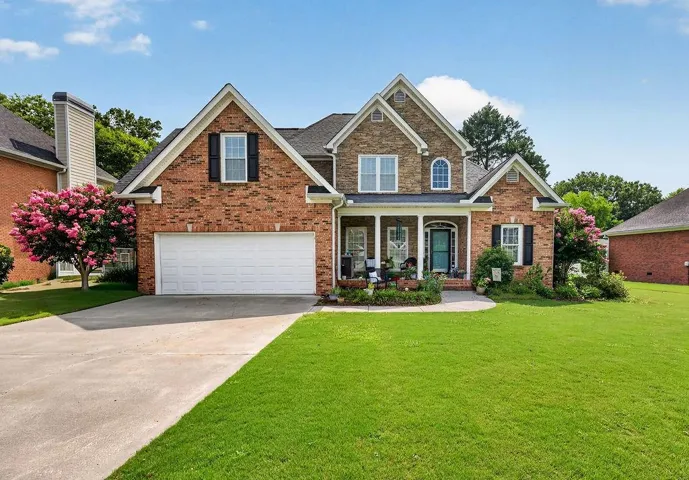 Traditional brick and stone exterior featuring a two-car garage, covered front porch with white columns, and a well-maintained lawn
