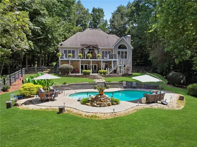 Elegant Colonial-style residence with expansive grounds featuring a resort-style swimming pool, integrated spa with stone surround, manicured lawn, mature tree-lined perimeter, and multi-level stone patio