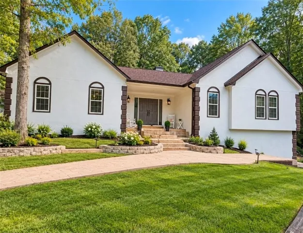 White stucco exterior with dark trim accents, gabled roofline, arched window details, double entry doors, and a terraced front walkway with retaining walls