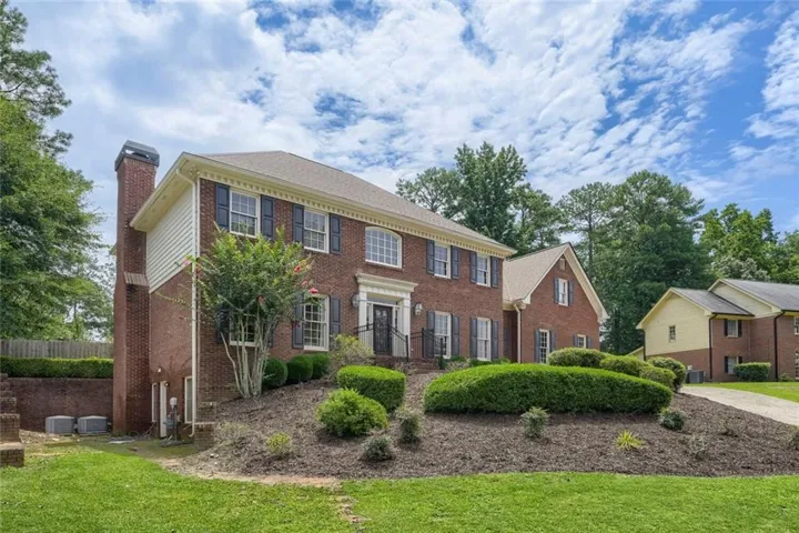 Brick exterior with white trim, black shutters, prominent front entry, and established landscaping