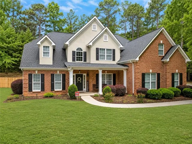 Brick and stucco exterior with dormer windows, a covered front porch, and a manicured lawn