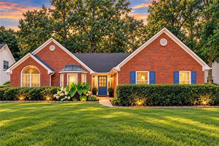 Red brick exterior with white trim, arched window, bay window, landscaped shrubbery, and a blue front door