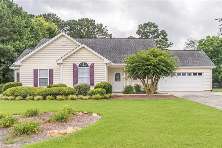 Ranch-style residence featuring light-colored siding, purple window shutters, a two-car garage, and a well-maintained lawn with established landscaping