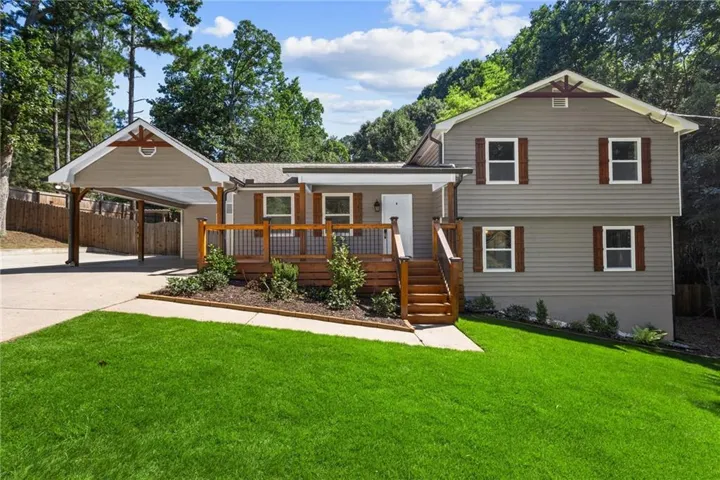Exterior featuring horizontal siding, a covered carport, wood-finish deck with railing, wood-finish shutters, and a well-maintained lawn